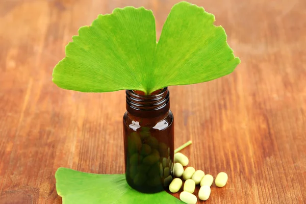 Ginkgo biloba hojas y frasco de medicina sobre fondo de madera — Foto de Stock