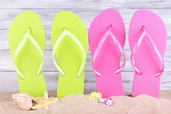 Heldere slippers op zand, op houten achtergrond — Stockfoto