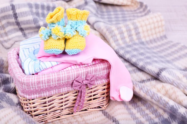 Baby clothes in basket on plaid in room — Stock Photo, Image