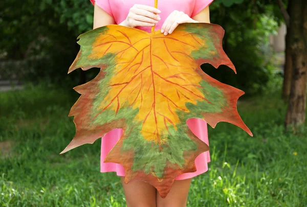 Girl holding decorative maple leaf in park — Stock Photo, Image