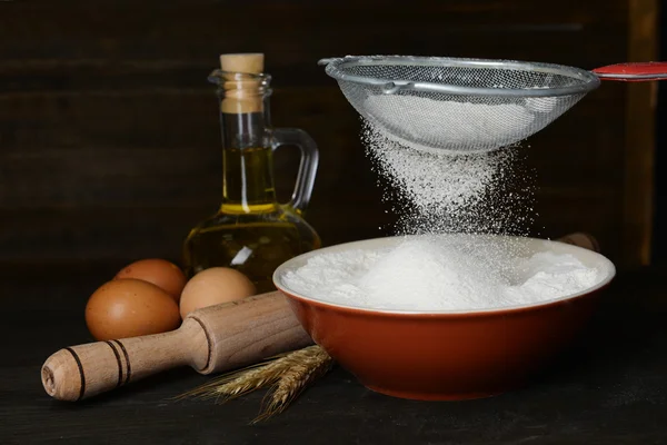 Sifting flour into bowl on table on wooden background — Stock Photo, Image