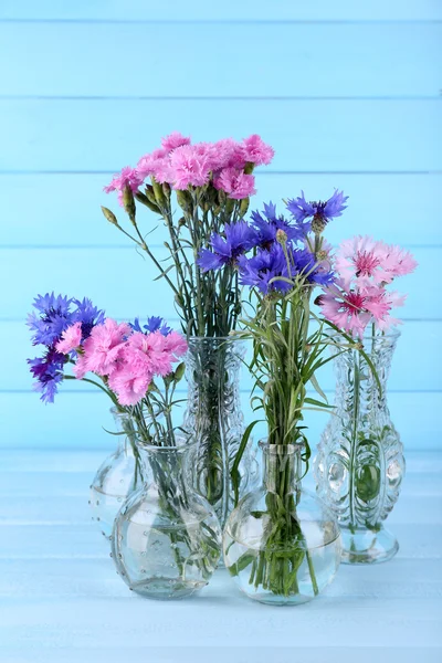 Schöne Sommerblumen in Vasen auf blauem Holzgrund — Stockfoto