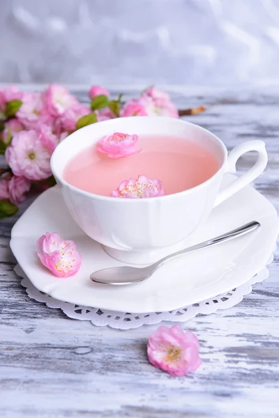 Beautiful fruit blossom with cup of tea on table on grey background — Stock Image Beautiful fruit blossom with cup of tea on table on grey background Stock Photo