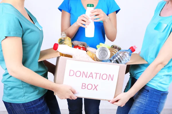 Vrijwilligers met donatiebox met levensmiddelen op grijze achtergrond Stockfoto