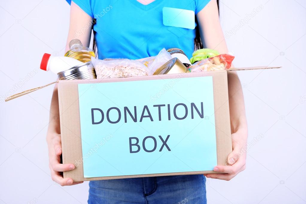 Volunteer with donation box with foodstuffs on grey background