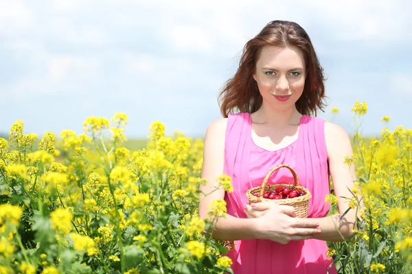 Piękna młoda kobieta trzyma Wiklinowy kosz z wiśniami w dziedzinie — Zdjęcie stockowe