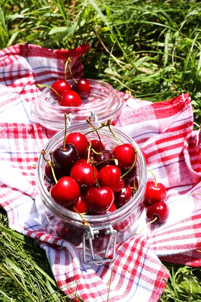 Sweet ripe cherries in glass jar, on napkin, on green grass background — Stock Photo, Image