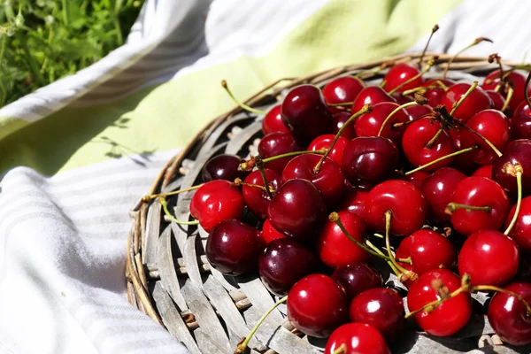 Cerises mûres sucrées sur tapis d'osier, sur fond d'herbe verte — Photo