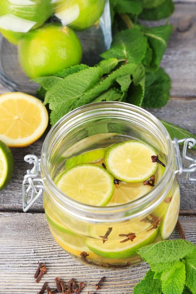 Inlagda limefrukterna och kryddnejlika i glasburk, på färg trä bakgrund — Stockfoto