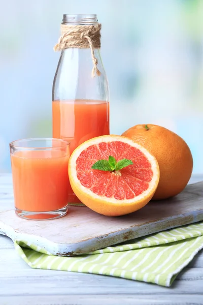 Спелые грейпфруты и свежий сок на разделочной доске, на деревянном фоне — стоковое фото