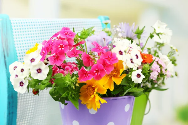 Bukett av färgglada blommor i dekorativa hinkar, på stol, på ljus bakgrund — Stockfoto