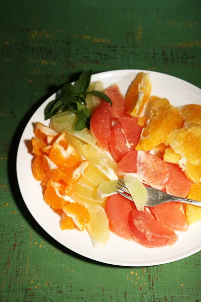 Sliced citrus fruits on plate, on wooden background — Stock Photo, Image