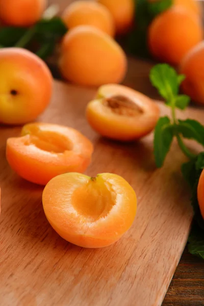 Ripe apricots with green mint leaves on cutting board, on wooden background — Stock Photo, Image