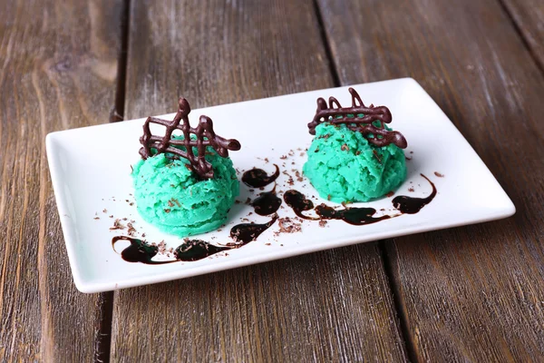 Tasty ice cream with chocolate decorations and sauce plate, on color wooden  background — Stock Photo, Image