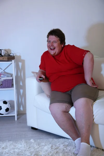 Lazy overweight male sitting on couch and watching television — Stock Photo, Image