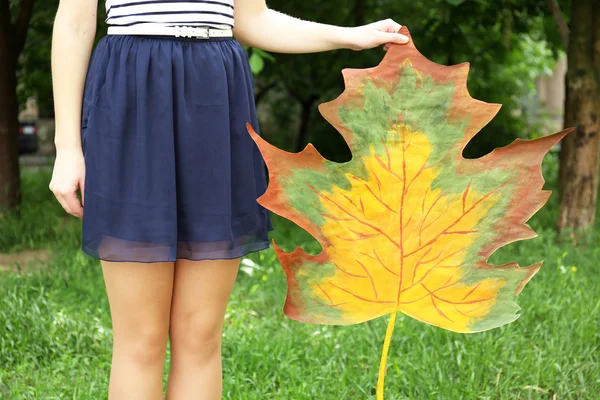 Girl holding decorative maple leaf in park — Stock Photo, Image