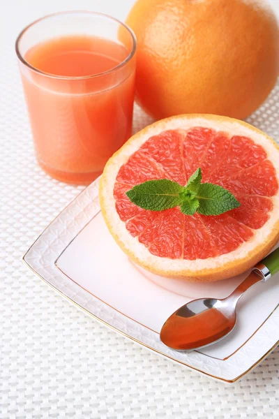 Die Hälfte der Grapefruit, ein Glas frischen Saft und ein Esslöffel auf dem Teller — Stockfoto