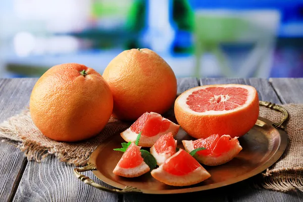 Спелые грейпфруты на подносе, на деревянном столе, на ярком фоне — стоковое фото