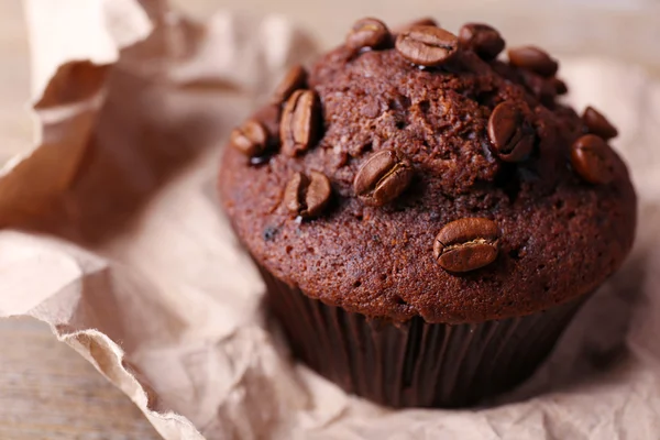 Schokoladenmuffin und Kaffeekörner auf Papier, auf Holzgrund — Stockfoto