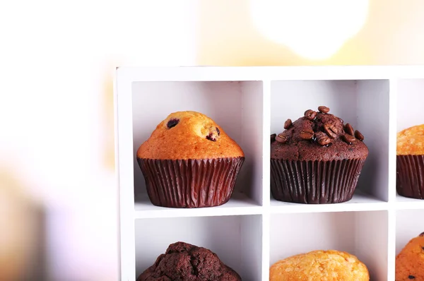 Tasty muffins on wooden shelves, on bright background — Stock Photo, Image