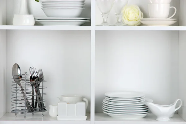 Different white clean dishes on wooden shelves — Stock Photo, Image