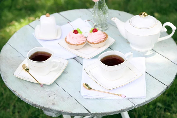 Coffee table with teacups and tasty cakes in garden — Stock Photo, Image