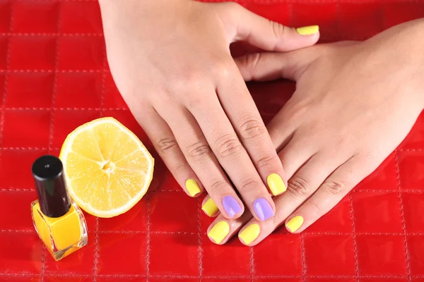 Female hand with stylish colorful nails holding fresh lemon — Stock Photo, Image