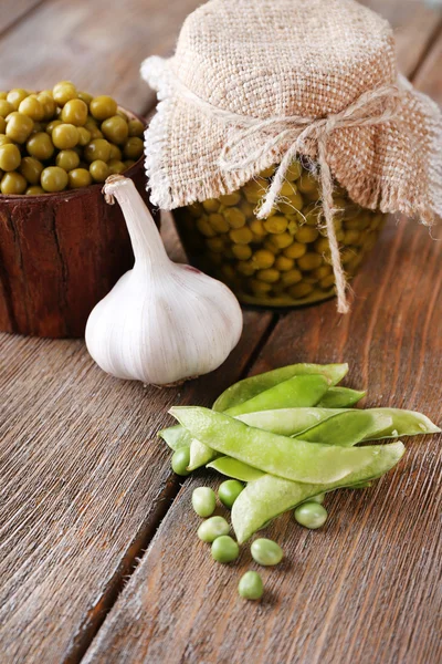 Fresh  and canned peas in bowl and glass jar on napkin, on wooden background — Stock Photo, Image