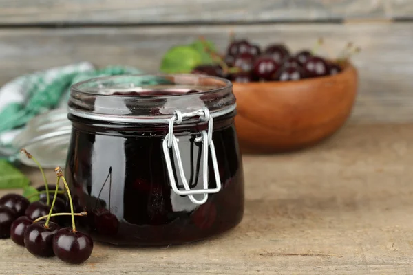 Sabrosa mermelada de cereza en tarro de vidrio sobre mesa de madera — Foto de Stock