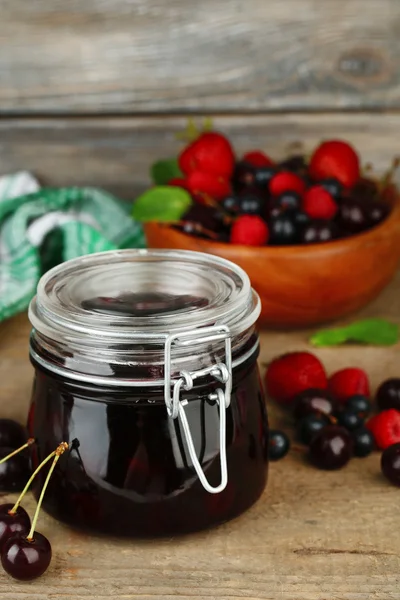 Tasty jam with berries in glass jar on wooden table — Stock Photo, Image