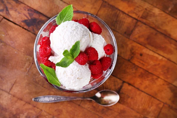 Helado cremoso con frambuesas en plato en cuenco de vidrio, sobre fondo de madera de color — Foto de Stock