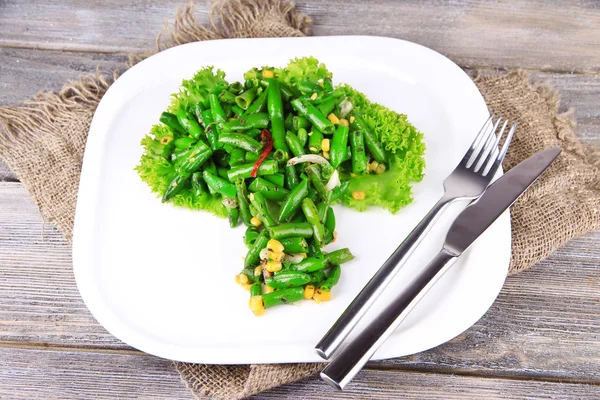 Salat mit grünen Bohnen, Schinken und Mais auf Teller, auf farbigem Holzgrund — Stockfoto