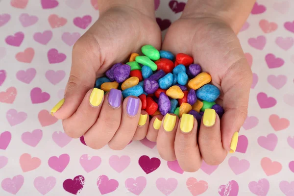 Mano femenina con elegantes uñas de colores sosteniendo caramelos de colores, sobre un fondo brillante — Foto de Stock