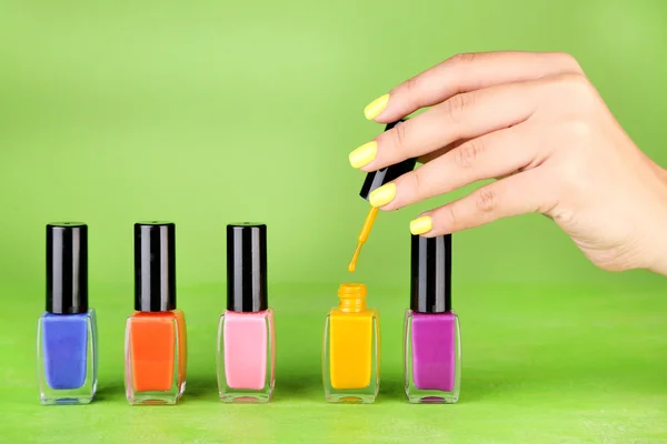 Mano femenina con elegantes uñas de colores sosteniendo botella con esmalte de uñas, sobre fondo verde —  Fotos de Stock