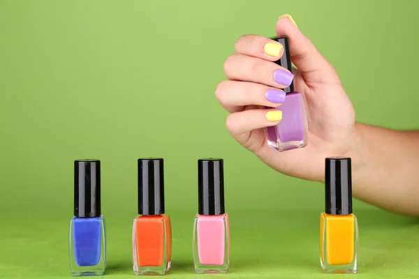 Kvinnlig hand med eleganta färgstarka naglar håller flaskan med nagellack, på grön bakgrund — Stockfoto
