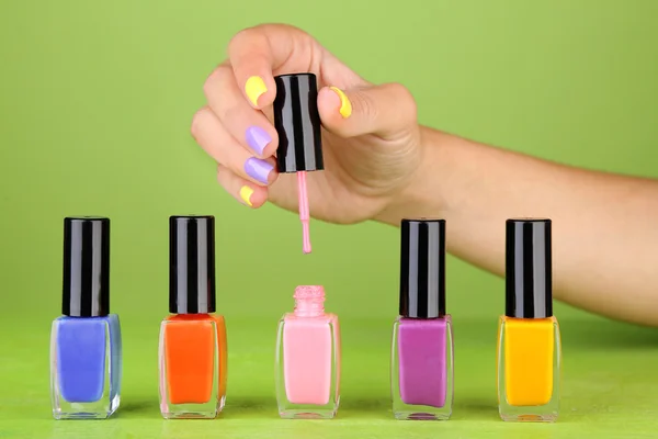 Mão feminina com unhas coloridas elegantes segurando garrafa com esmalte, no fundo verde — Fotografia de Stock