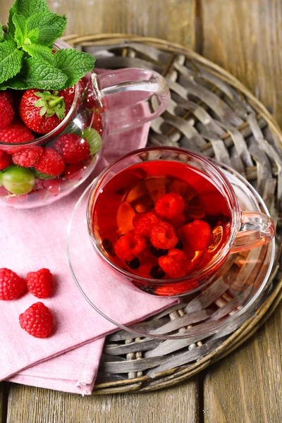 Tè rosso frutta con frutti di bosco in tazza di vetro, su sfondo di legno — Foto Stock
