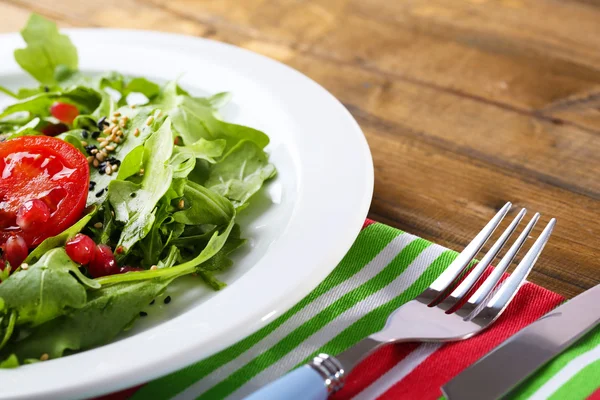 Grön sallad med rucola, tomater och sesam på plattan, på trä bakgrund — Stockfoto
