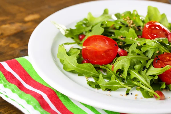 Grön sallad med rucola, tomater och sesam på plattan, på trä bakgrund — Stockfoto