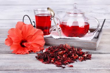 Hibiscus tea in glass teapot and flower on color napkin on wooden background clipart