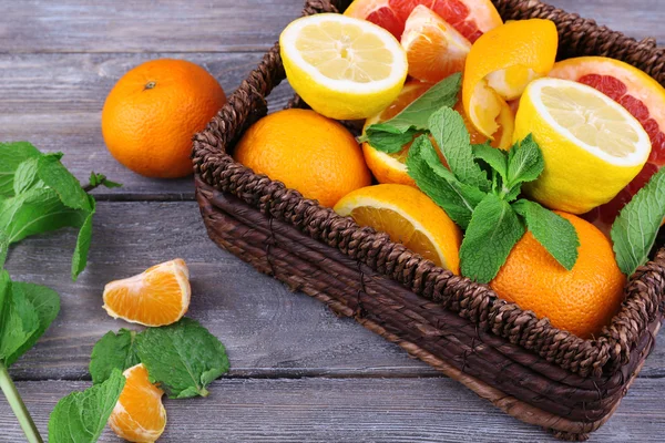 緑の葉の枝編み細工品バスケットに木製の背景を持つ新鮮な柑橘系の果物 — ストック写真