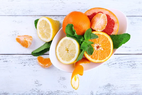 Färska citrusfrukter med gröna blad i skål på trä bakgrund — Stockfoto