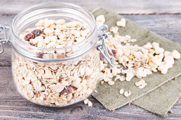 Granola fatta in casa in vaso di vetro, su sfondo di legno a colori — Foto Stock