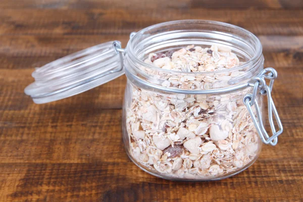 Granola fatta in casa in vaso di vetro, su sfondo di legno a colori — Foto Stock