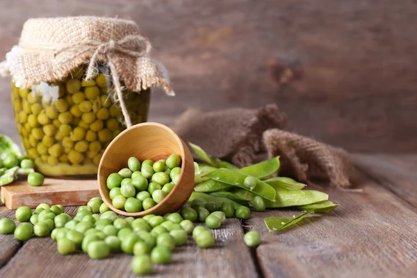 Fresh  and canned peas in bowl and glass jar on napkin, on wooden background — Stock Photo, Image