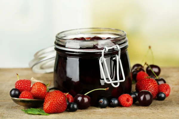 Smakelijke jam met bessen in glazen pot op houten tafel — Stockfoto