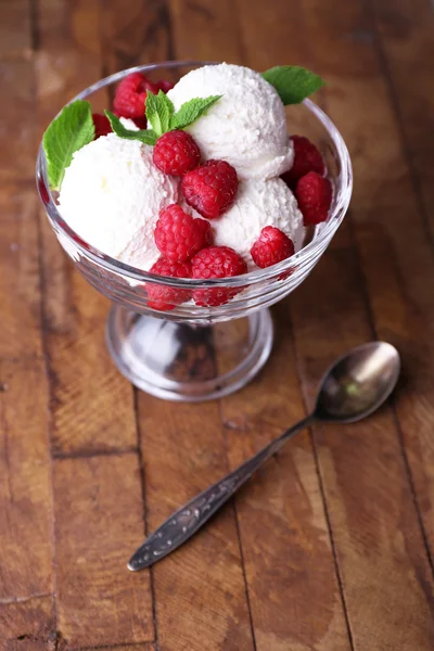 Gelato cremoso con lamponi su piatto in ciotola di vetro, su sfondo di legno a colori — Foto Stock