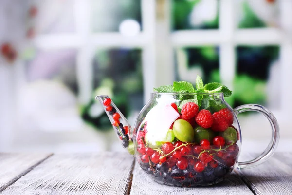 Skogsbär och myntablad i glas Tekanna, på träbord, på ljus bakgrund — Stockfoto