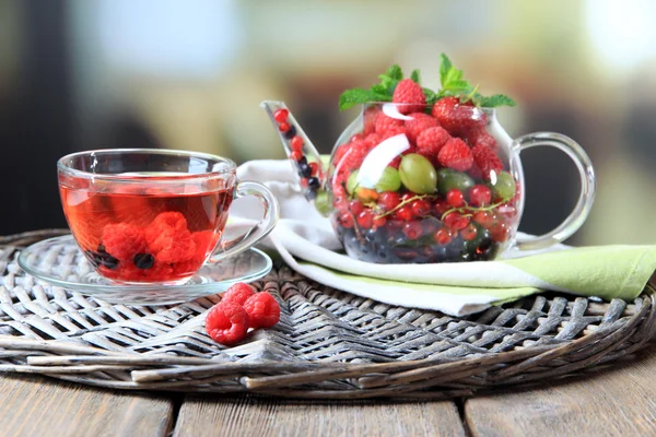 Té rojo de frutas con bayas silvestres en taza de vidrio, sobre mesa de madera, sobre fondo brillante — Foto de Stock