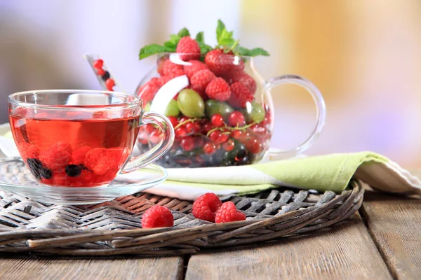 Teh merah buah dengan buah-buahan liar dalam gelas, di atas meja kayu, dengan latar belakang cerah — Stok Foto